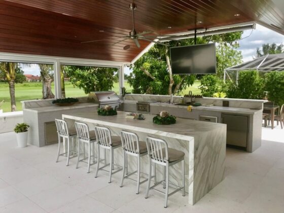 outdoor kitchen with marble countertop island, bar seating, built-in grill and covered patio entertainment area