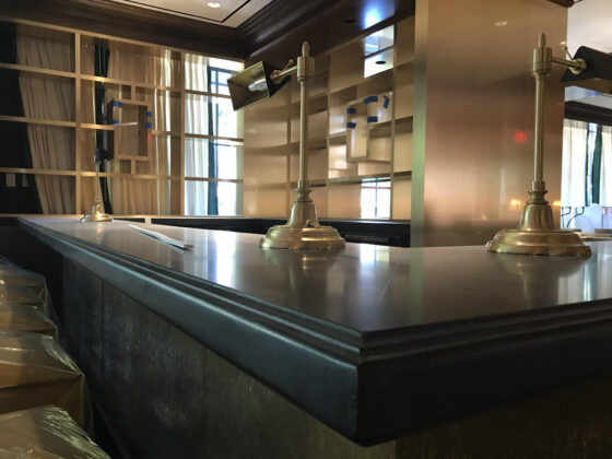 commercial bar counter with dark stone countertop and brass desk lamps in upscale restaurant interior
