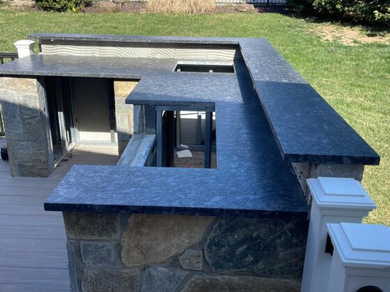 Outdoor kitchen installation with dark stone countertops and custom stone base on residential deck patio