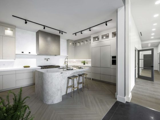 Modern luxury kitchen featuring a curved marble waterfall island, minimalist grey cabinetry, and herringbone wood flooring.