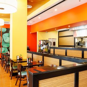 modern restaurant interior with wood panel counters, orange walls, dining tables and open kitchen service area