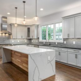 modern kitchen with waterfall quartz island gray cabinets stainless steel appliances and tile backsplash