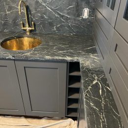 dark marble countertop and backsplash with white veining brass sink and faucet in modern bar or kitchenette design