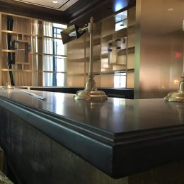 commercial bar counter with dark stone countertop and brass desk lamps in upscale restaurant interior