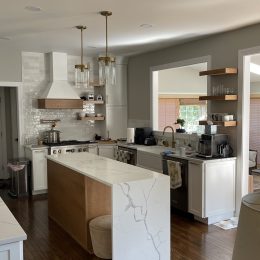 modern kitchen with waterfall quartz island white cabinetry wood accents and pendant lighting