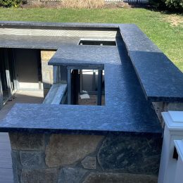 Outdoor kitchen installation with dark stone countertops and custom stone base on residential deck patio