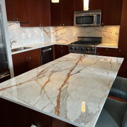 Modern kitchen with marble-style quartz island countertop, matching backsplash, and dark wood cabinetry