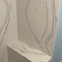 Custom quartz shower wall and bench with white surface and dramatic grey veining for modern bathroom design