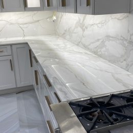 white marble kitchen countertop and full slab backsplash with gray veining modern cabinets and gas cooktop