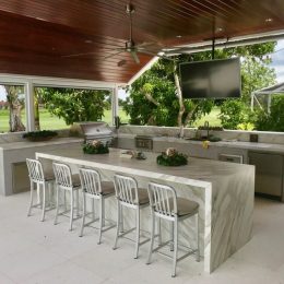 luxury outdoor kitchen with marble waterfall island, bar seating and built-in grill under covered patio